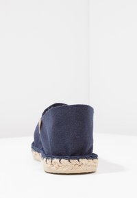 Marineblaue Canvas-Espadrilles mit einer Sohle aus Jute-Seil. Verfügt über einen abgerundeten Rücken und ein kleines Lederakzentetikett nahe der Ferse. Einfaches Design.