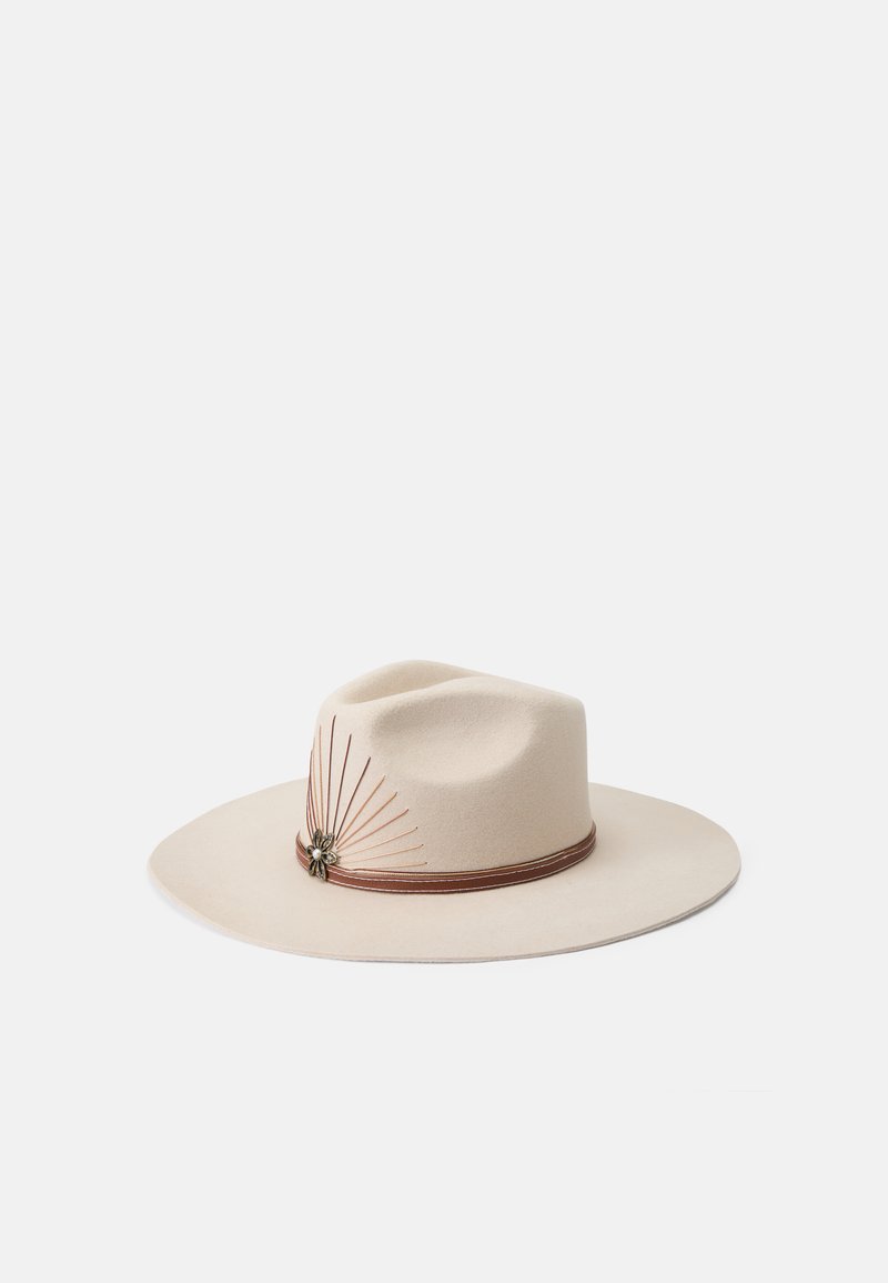 Chapéu de feltro bege de aba larga com uma coroa arredondada, apresentando uma faixa de couro marrom e acentos metálicos decorativos com espigões finos.