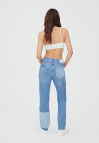 Jean en denim bleu clair avec un design patchwork, présentant un mélange de nuances plus foncées et plus claires, des poches standard, et une taille haute.