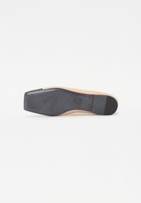 Semelle noire avec des rainures horizontales, intersemelle beige, et un bord supérieur lisse et courbé. Présente un petit accent noir au niveau des orteils pour plus de détail.