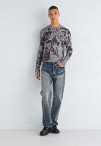 Long-sleeve gray T-shirt with artistic black text and graphic patterns, paired with light blue jeans and black shoes.