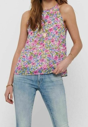 Frau trägt ein ärmelloses florales Neckholder-Top mit pinken, lila und blauen Blumen, kombiniert mit hellblauen Jeans und goldenen Schmuck.