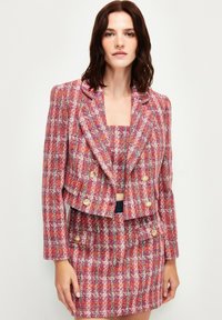 Roze en rode tweed blazer met gouden knopen, cropped ontwerp en een bijpassende mini rok. De stof heeft een gestructureerd patroon.