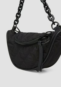 Czarna torba na ramię z pikowanego materiału o zaokrąglonym kształcie, z zamkiem błyskawicznym na górze i grubym łańcuszkiem. Posiada gładką teksturę i minimalną ilość elementów metalowych.