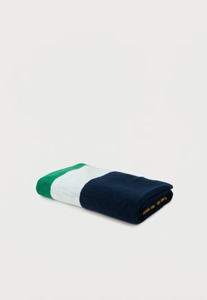 Serviette pliée avec des blocs de couleurs vert, blanc et bleu marine sur un fond gris clair uni.