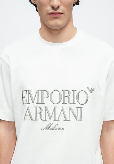 Biele bavlnené tričko s veľkým sivým vyšívaným logom "EMPORIO ARMANI" a menším nápisom "Milano" pod ním, s okrúhlym výstrihom.