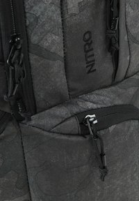 Schwarzer Rucksack aus strukturiertem Stoff mit einem dezenten Muster. Reißverschlüsse und Beschläge in Schwarz, mit schräge Taschen und verstellbaren Trägern.