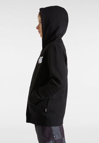 Sudadera con capucha negra, con un bolsillo frontal y costuras laterales, que presenta un logo impreso en el pecho. Tejido suave con una textura lisa.