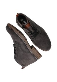 Grå ruskindsko med en brun læderdetalje, der har runde snørebånd, en tekstureret gummisål og en syet detalje omkring kanten.