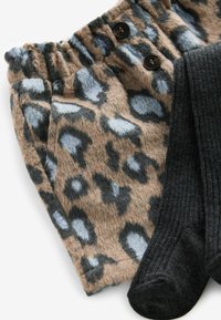 Spodnie w leopardzi wzór w kolorze beżowym i niebieskim z dwóch ciemnych guzików w pasie, połączone z ciemnoszarymi skarpetkami w prążki.