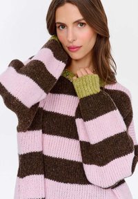 Sweter w paski w różowym i ciemnobrązowym kolorze z zielonym ściągaczem przy kołnierzyku i mankietach, charakteryzujący się luźnym, teksturowanym splotem.