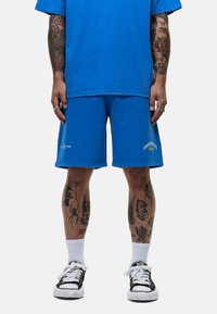 T-shirt en coton bleu et shorts bleus assortis, tous deux présentant un léger effet usé. Les détails incluent une broderie blanche et une coupe décontractée.