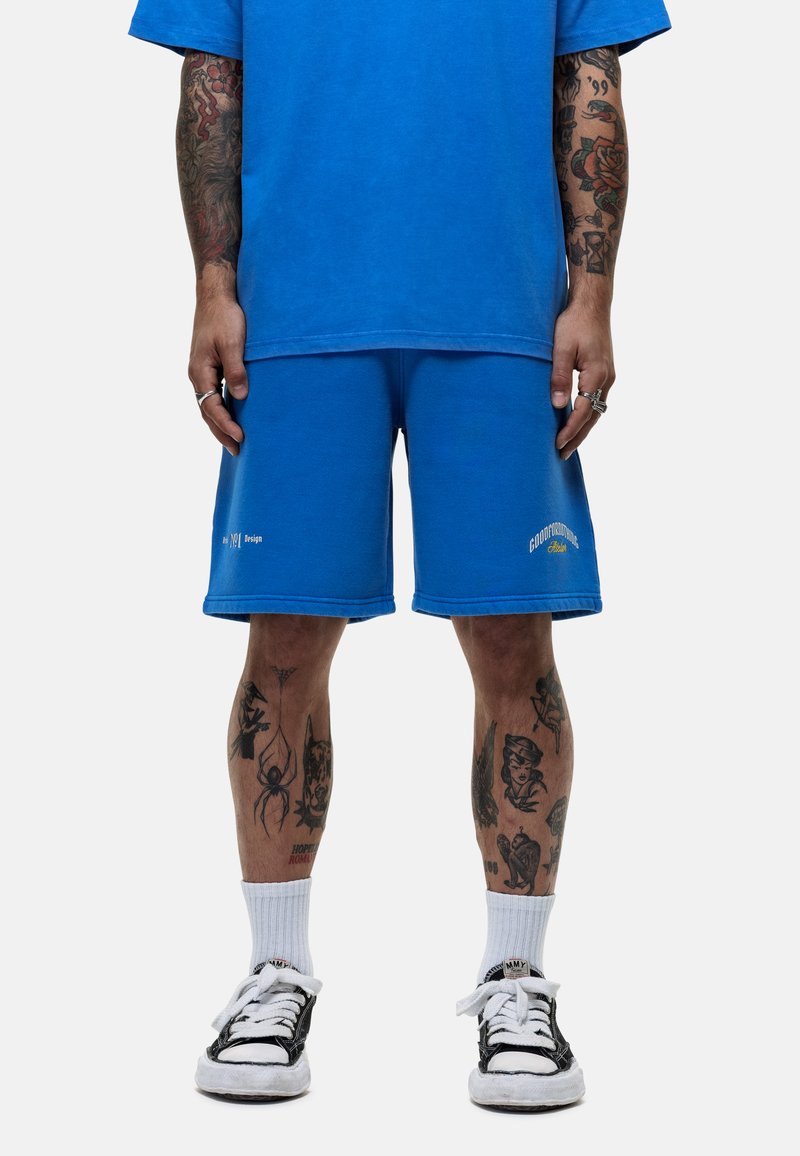 T-shirt en coton bleu et shorts bleus assortis, tous deux présentant un léger effet usé. Les détails incluent une broderie blanche et une coupe décontractée.
