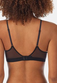 Donna con capelli ricci vista di spalle, indossa un reggiseno nero con spalline regolabili e chiusura posteriore a gancio.