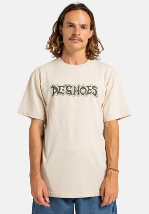 Crème-kleurig katoen t-shirt met korte mouwen en een ronde halslijn, voorzien van een donker grafisch logo "DE SHOES" over de borst.