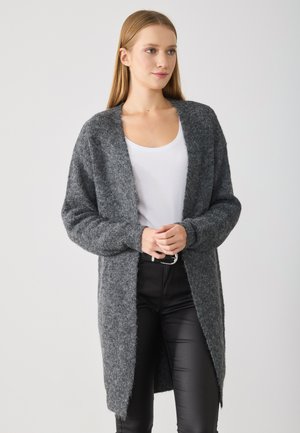Grå strikket cardigan med lange ermer og åpen front, med en myk, teksturert overflate og litt lengre bakhem. Brukt over en hvit topp.