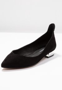 Chaussure plate en daim noir avec un bout pointu et un petit talon argenté brillant. Présente une coupe basse et une doublure intérieure lisse.