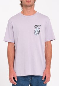 T-shirt en coton violet clair avec un col rond. Présente un petit imprimé graphique sur la poitrine gauche et des manches courtes. Coupe classique.