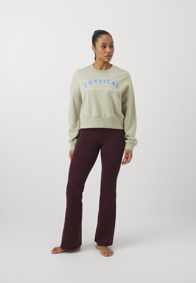 Khaki cropped sweatshirt with blue "PHYSICAL EDUCATION" lettering, paired with dark burgundy flared pants, both in smooth fabric.