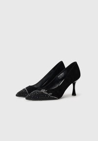 Black suede heels featuring a pointed toe, embellished with rhinestones and a curved accent. Approximate heel height of 5 cm.