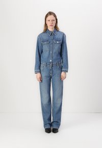 Τζιν ολόσωμο φόρεμα σε ανοιχτό μπλε χρώμα, με δύο τσέπες στο στήθος, κλείσιμο με κουμπιά και ευθεία γραμμή. Λείο υφή και κλασικό στυλ.