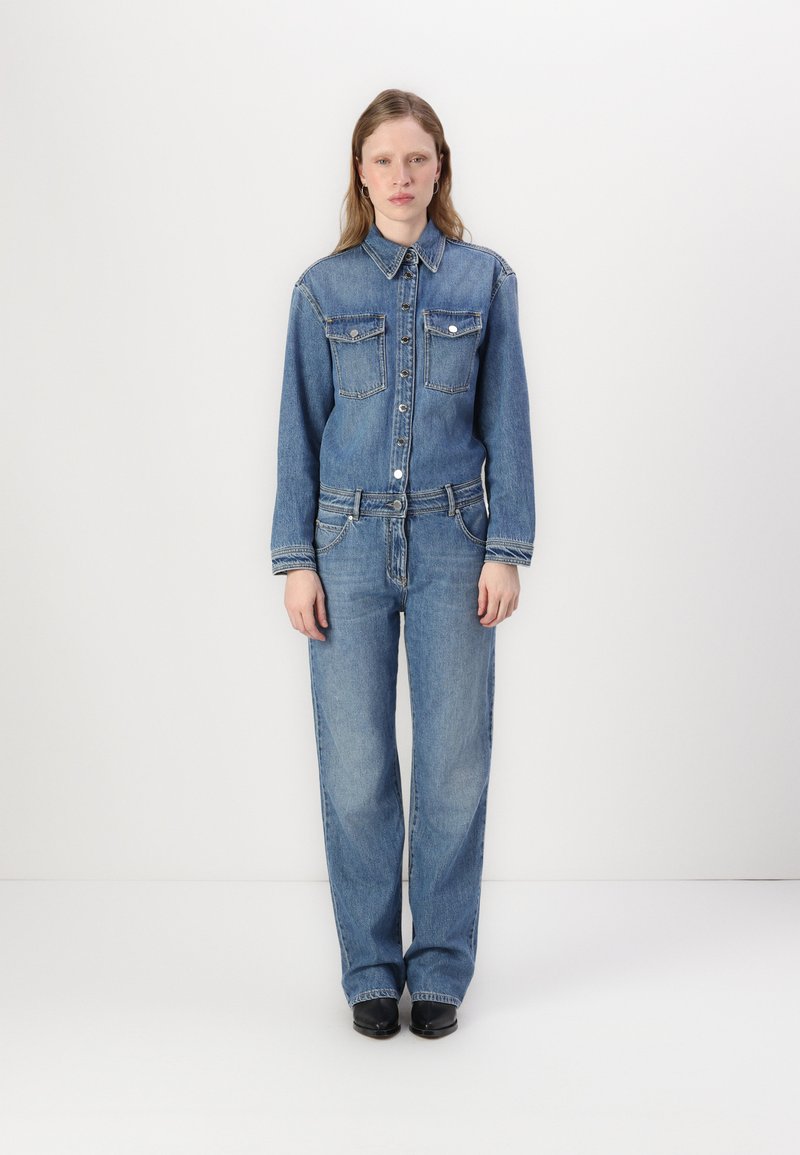 Τζιν ολόσωμο φόρεμα σε ανοιχτό μπλε χρώμα, με δύο τσέπες στο στήθος, κλείσιμο με κουμπιά και ευθεία γραμμή. Λείο υφή και κλασικό στυλ.