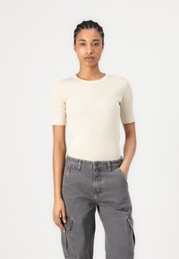 Light beige ribbed short-sleeve top with a round neckline, paired with gray cargo pants featuring pockets and a relaxed fit.