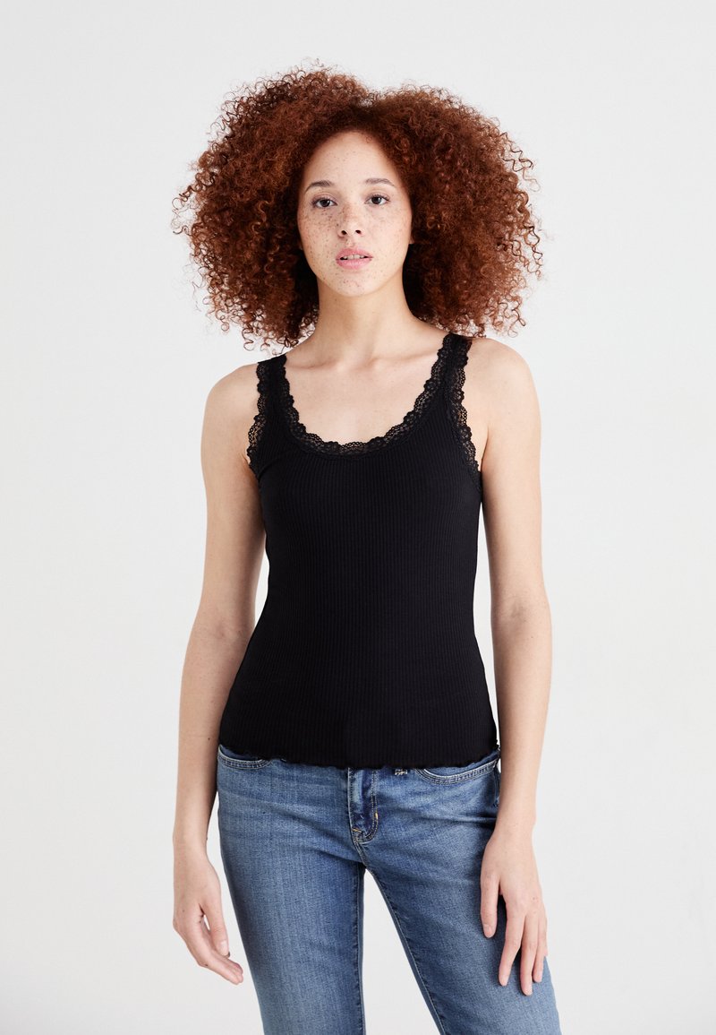 Top aderente nero in maglia a costine con bordino in pizzo lungo il collo e le spalline. Progettato con una forma aderente e orlo scallop. Indossato con jeans blu.