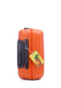 Valise rigide orange avec une surface texturée, dotée d'une poignée noire, d'une double fermeture éclair et d'une étiquette colorée en forme d'ananas attachée.