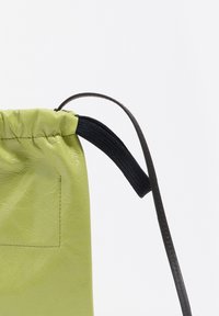 Bolso verde de cuero texturizado con cierre de cordón, con una correa negra tejida y un pequeño bolsillo exterior.