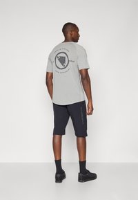 T-shirt gris clair avec un graphique noir au dos, associé à un short sombre avec un logo sur le côté, conçu pour le confort et les activités sportives.