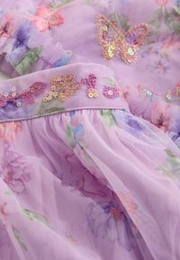 Tela de tul lila con patrones florales y apliques intrincados de mariposas. Presenta detalles con lentejuelas y una cintura fruncida.