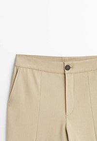 Beiget räätälöidyt housut, joissa on sileä pinta, etutaskut ja nappikiinnitys. Vyötäröllä on siisti viimeistely ja hienovaraiset saumat.