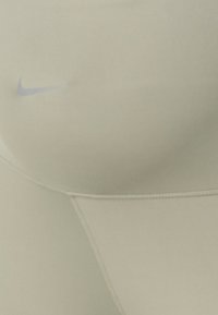 Nike svijetlosmeđi tajice s glatkom površinom, sa suptilnim šavovima i malim plavim logotipom na pojasu.