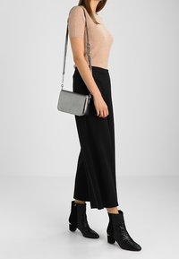 Pantaloni neri a gamba larga abbinati a un top corto a maniche corte color beige a coste. Accessoriati con una borsa d'argento e stivaletti neri a caviglia texturizzati.