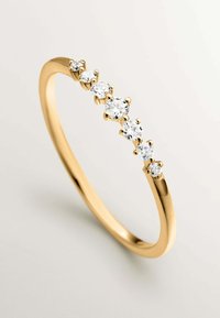 Anillo de oro con cinco piedras preciosas redondas y transparentes en un engaste de garras a lo largo de la banda, con una superficie lisa y pulida y un diseño esbelto.