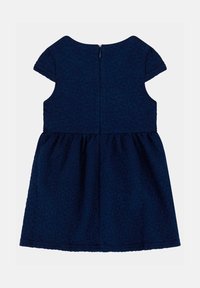 Marineblaues Kleid mit einer strukturierten Musterung, kurzen Puffärmeln und einem gerafften Rock. Verfügt über einen Reißverschluss auf der Rückseite.
