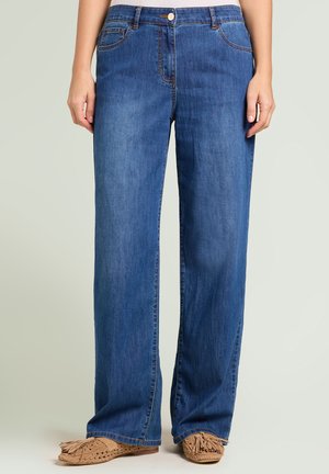 Jean en denim bleu à taille moyenne et jambes larges porté avec des mocassins beiges tissés de style mocassin avec des détails à franges.