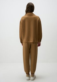 Un haut marron surdimensionné à manches longues avec un col de chemise, associé à un pantalon ample assorti. Les deux éléments ont une texture douce et des poignets élastiques.