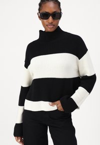 Maglione a righe bianche e nere in maglia, con collo alto, texture a costine e maniche lunghe. Vestibilità ampia con un design corto.