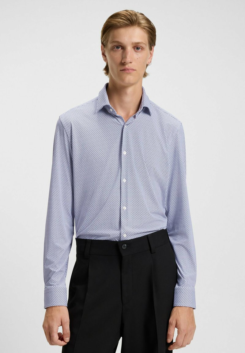 Helles blaues gemustertes Hemd mit Button-Down-Kragen, langen Ärmeln und schwarzen Anzughosen. Besitzt kleine geometrische Designs auf der gesamten Fläche.