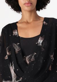 Fekete, átlátszó ruházat, madármintákkal, mély V-nyakkal és sima, könnyű textúrával. Belső rétege egy fekete tanktop.