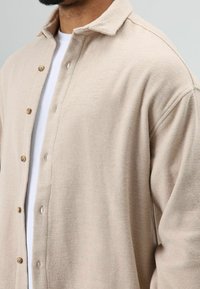 Beige overhemd met knopen, gemaakt van zachte stof, met een kraag, houten knopen en een losse pasvorm met zichtbare stikseldetails.