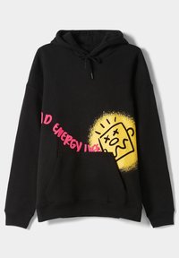 Sudadera negra con bolsillo frontal, texto rosa "Buena Energía" en diagonal y gráfico amarillo de una cara abstracta sonriente en el frente.