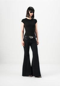 T-shirt nera aderente, jeans svasati neri con cintura in metallo argentato. Occhiali da sole, capelli lisci. Sfondo semplice e minimalista.