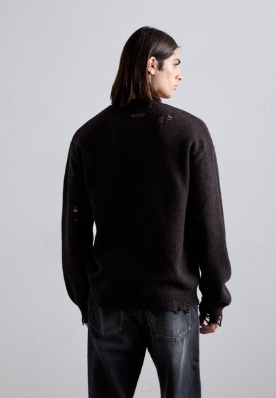 Dunkelbrauner Pullover aus strukturiertem Material, mit abgenutzten Flicken auf dem Rücken, runder Ausschnitt und gerippten Bündchen.