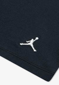 Tissu noir à texture lisse avec un logo Jumpman brodé en blanc. Design simple, détails de couture minimalistes.