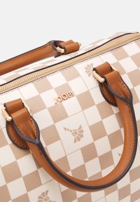 Ruskea ja kerma-valkoinen ruudullinen laukku, jossa on nahkaiset kahvat, kultainen vetoketju ja hienovaraiset logoyksityiskohdat; laukulla on jämäkkä muoto ja teksturoitu pinta.