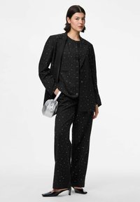 Juodas kostiumas su taškeliais. Atsipalaidavęs švarkas su išpjautomis apykaklėmis ir mygtukais, derinamas su tiesaus kirpimo kelnėmis. Sidabrinė rankinė.