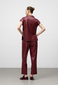 Top e pantaloni in ecopelle bordeaux con zip sul retro, maniche corte e vestibilità comoda. Indossati con sneakers bordeaux abbinate.